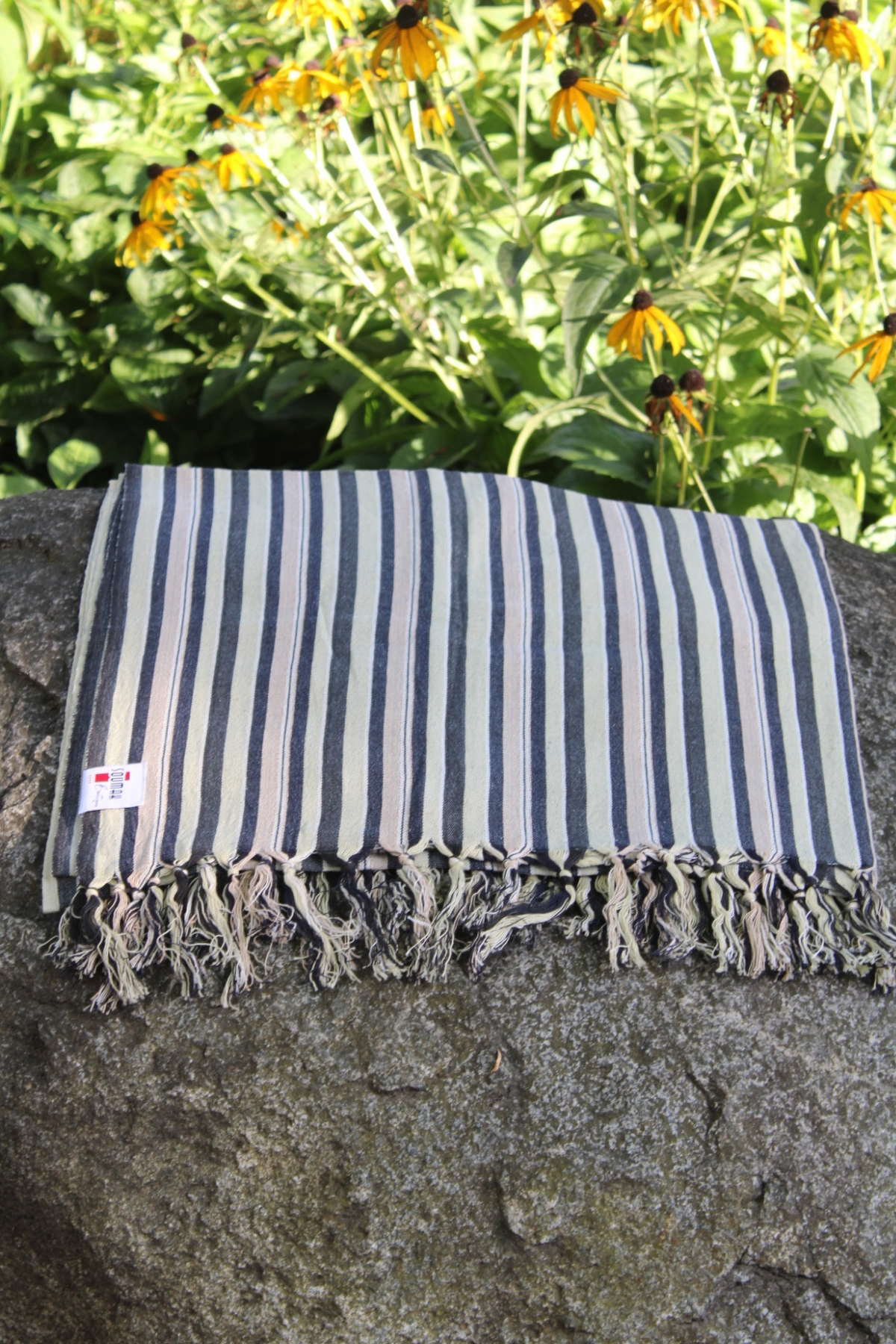 Striped towel with tassels on a stone surface with flowers in the background