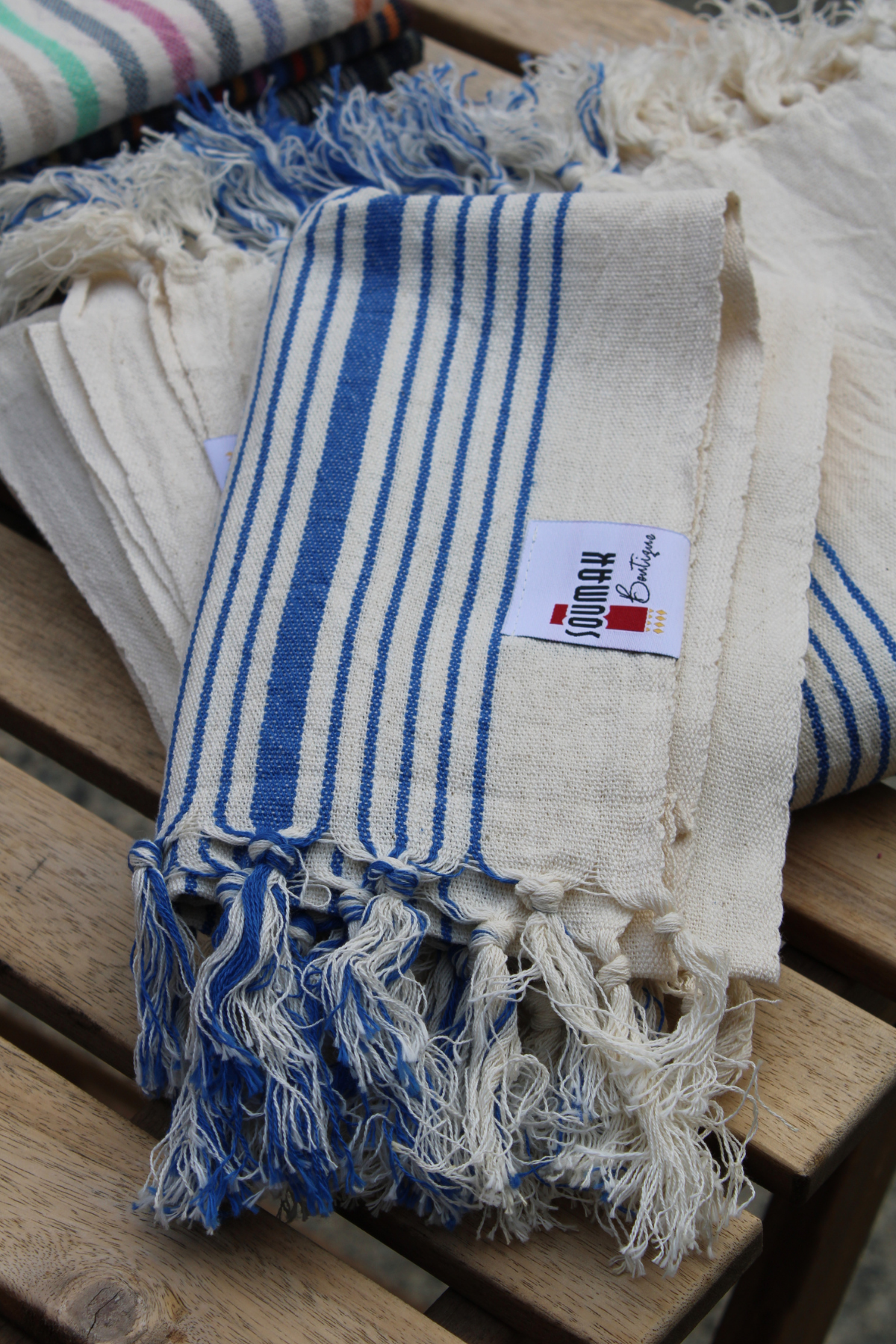 Display the elegance of our Organic Turkish Hand Towel, stylishly placed on top of our Turkish Bath Towel, featuring beautiful tassels. This high-quality design in white with blue stripes is available at Soumak Boutique, Vancouver, BC, Canada, inside the Kids Market on Granville Island.