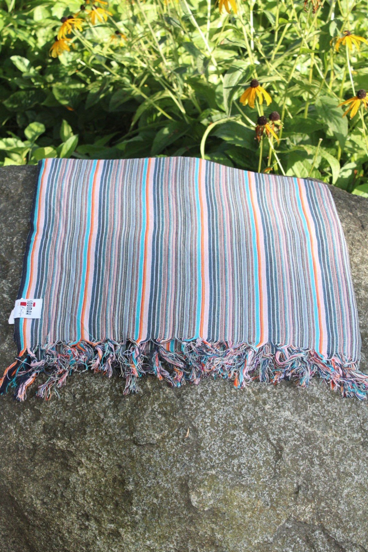 Striped fabric with frayed edges on a rock with greenery in the background