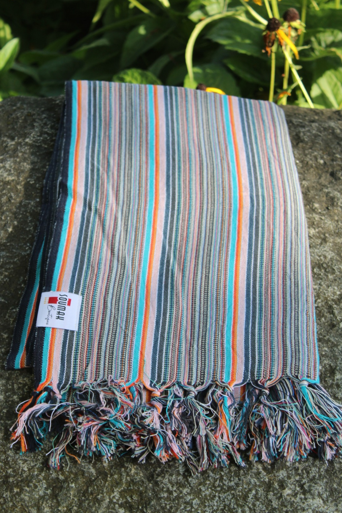 Striped towel with fringes on a stone surface with greenery in the background