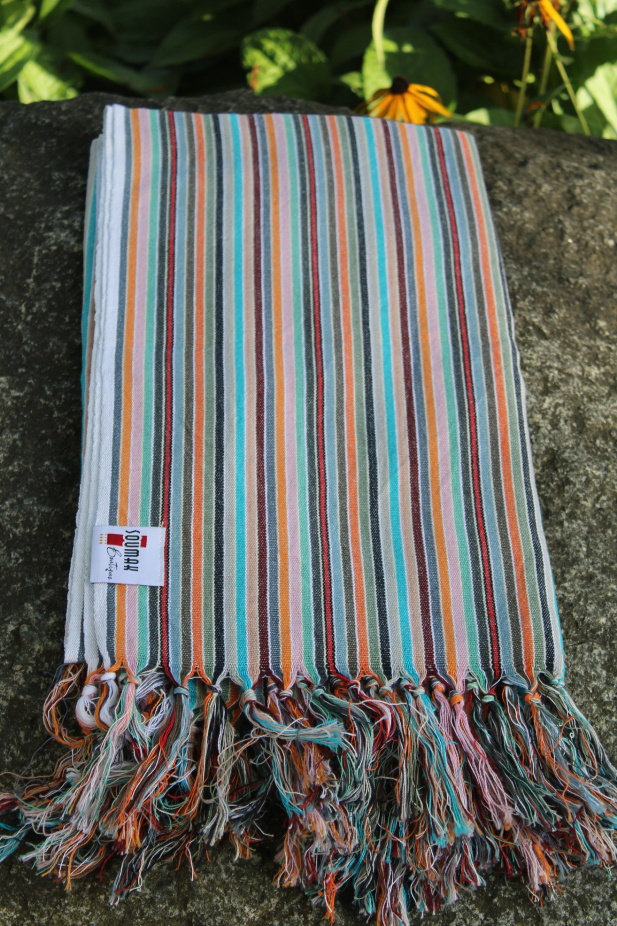 Striped towel with fringes on a stone surface with greenery in the background