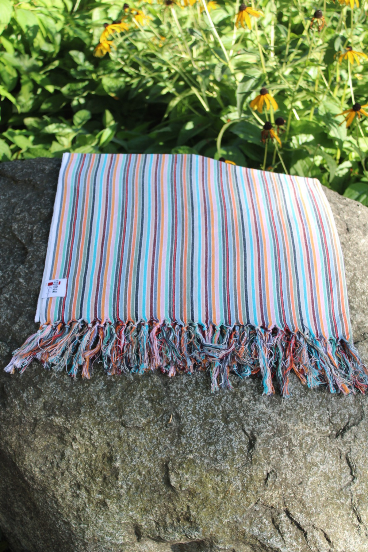 Striped towel on a rock with greenery and flowers in the background